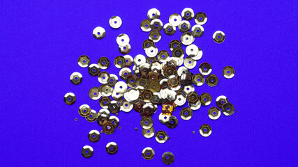 Pile of golden sequins on blue background, top view