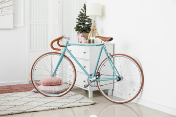 Fototapeta na wymiar Bicycle near chest of drawers with Christmas tree and lamp in living room