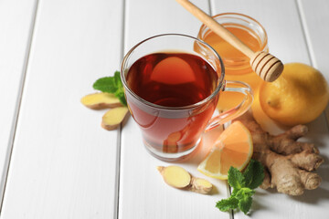 Cup of delicious ginger tea and ingredients on white wooden table