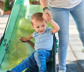 Fototapeta na wymiar Mother and son smiling confident playing on slide at park playground