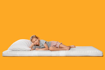 Little girl lying on comfortable mattress against orange background, space for text