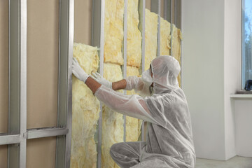 Worker in uniform and respiratory mask insulating wall indoors