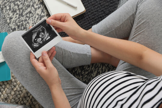 Pregnant woman holding ultrasound photo of baby, top view