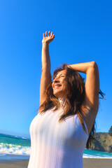 Woman raising her hand to the sun enjoying the sun at the beach