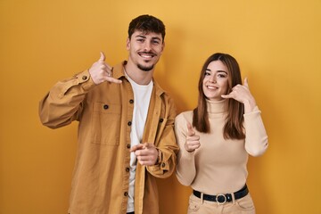 Young hispanic couple standing over yellow background smiling doing talking on the telephone...