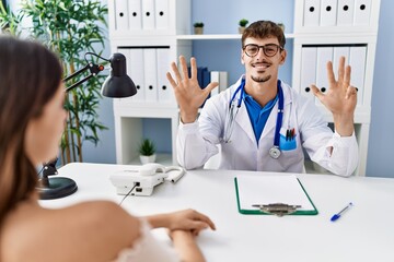 Young doctor with client at medical clinic showing and pointing up with fingers number nine while smiling confident and happy.