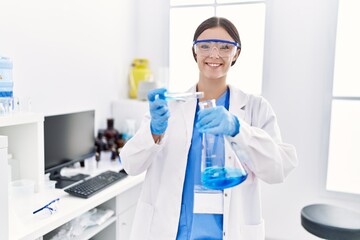 Fototapeta premium Young hispanic woman wearing scientist uniform holding test tube at laboratory