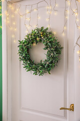 White door with Christmas mistletoe wreath and glowing lights in hall