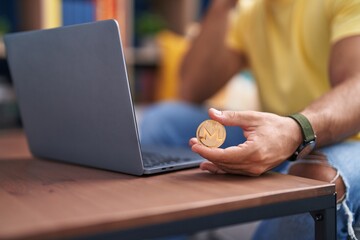 Young hispanic man holding monero crypto currency using laptop at street