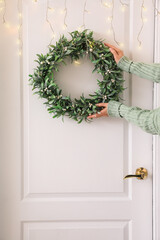 Woman hanging Christmas mistletoe wreath on white door in hall