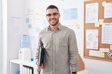 Young hispanic man business worker smiling confident holding binder at office