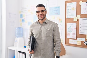 Fototapeta premium Young hispanic man business worker smiling confident holding binder at office