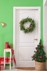 White door with Christmas wreath and fir tree in hall