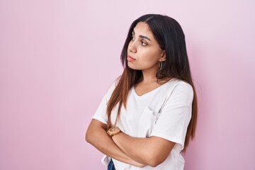 Young arab woman standing over pink background looking to the side with arms crossed convinced and confident