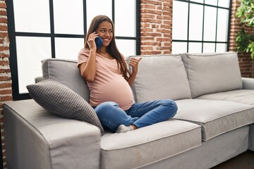 Obraz premium Young pregnant woman having conversation speaking on the smartphone pointing thumb up to the side smiling happy with open mouth