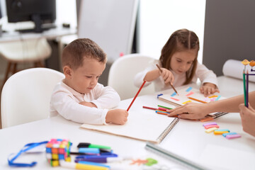 Adorable girl and boy drawing on notebook sitting on table at kindergarten