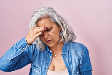 Middle age woman with grey hair standing over pink background tired rubbing nose and eyes feeling fatigue and headache. stress and frustration concept.