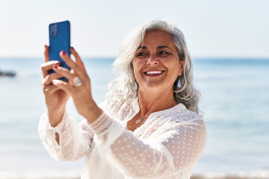 Middle age woman smiling confident making selfie by the smartphone at seaside