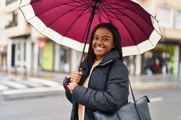African american woman smiling confident using umbrella at street