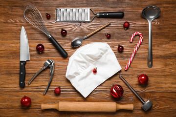 Chef's hat with utensils, candy cane and Christmas balls on wooden background