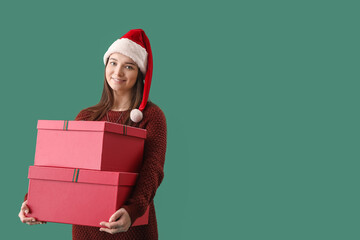 Young woman in Santa hat with Christmas gifts on green background