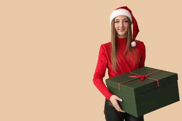 Young woman in Santa hat with Christmas gift on beige background