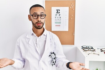 Fototapeta na wymiar African american optician man standing by eyesight test clueless and confused with open arms, no idea concept.