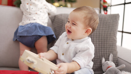 Fototapeta premium Adorable toddler holding tambourine sitting on sofa by christmas tree at home
