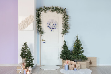White door with Christmas wreath, fir branches, trees and presents in hall