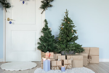 Small Christmas trees with presents near white door in hall