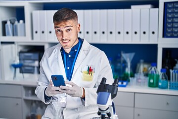 Fototapeta na wymiar Young hispanic man scientist using smartphone at laboratory