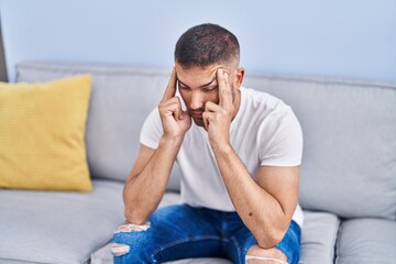 Young hispanic man stressed sitting on sofa at home