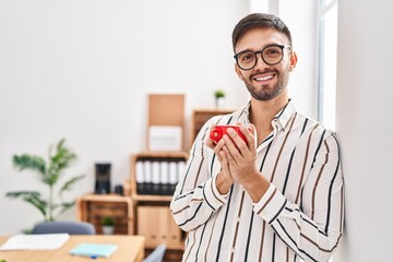 Young hispanic man business worker smiling confident drinking coffee at office