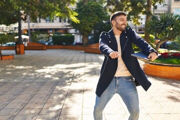 Young hispanic man holding laptop dancing at park