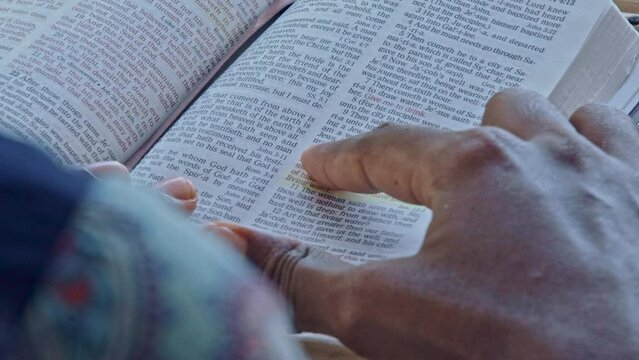 A lady's fingers points to Bible verses while she reads the page.