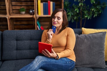 Middle age woman using laptop and credit card sitting on sofa at home