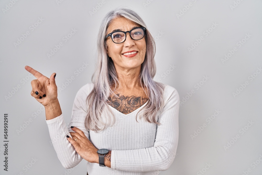 Wall mural middle age woman with grey hair standing over white background with a big smile on face, pointing wi