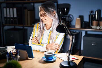 Middle age woman with grey hair working at the office at night happy face smiling with crossed arms looking at the camera. positive person.