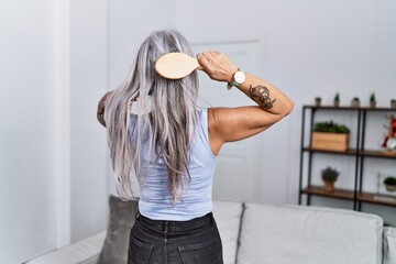 Middle age grey-haired woman on back view combing hair standing at home