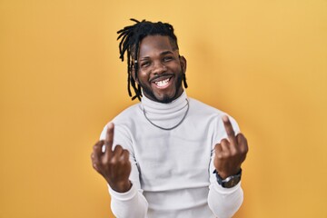 African man with dreadlocks wearing turtleneck sweater over yellow background showing middle finger doing fuck you bad expression, provocation and rude attitude. screaming excited