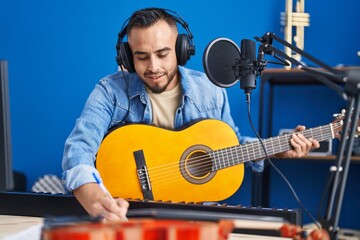 Young hispanic man artist composing song playing classical guitar at music studio