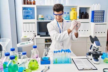Fototapeta premium Young hispanic man wearing scientist uniform writing on test tube at laboratory