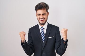 Young hispanic man with tattoos wearing business suit and tie celebrating surprised and amazed for success with arms raised and eyes closed. winner concept.