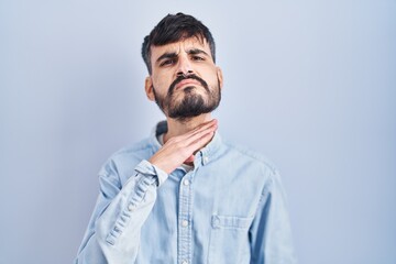 Young hispanic man with beard standing over blue background cutting throat with hand as knife, threaten aggression with furious violence