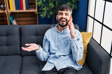 Young hispanic man talking on the smartphone sitting on sofa at home