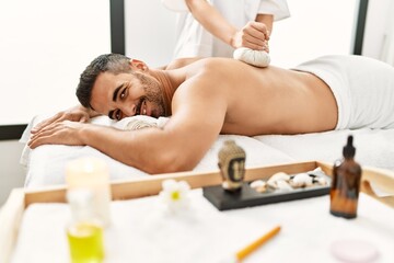 Obraz na płótnie Canvas Young hispanic man having back massage using thai bags at beauty center