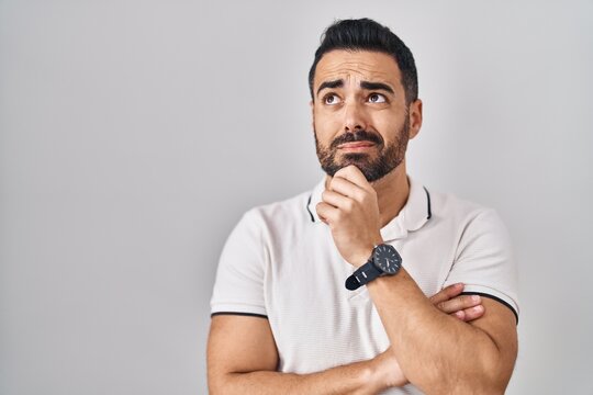 Young hispanic man with beard wearing casual clothes over white background thinking worried about a question, concerned and nervous with hand on chin