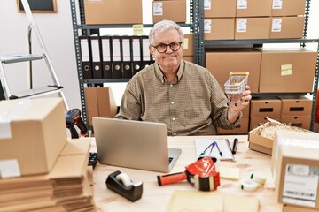 Senior caucasian man working at small business ecommerce holding shopping cart looking positive and happy standing and smiling with a confident smile showing teeth