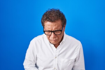 Middle age hispanic man standing over blue background with hand on stomach because indigestion, painful illness feeling unwell. ache concept.