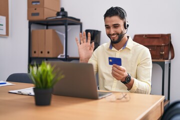 Hispanic young man wearing call center agent headset doing online shopping looking positive and happy standing and smiling with a confident smile showing teeth